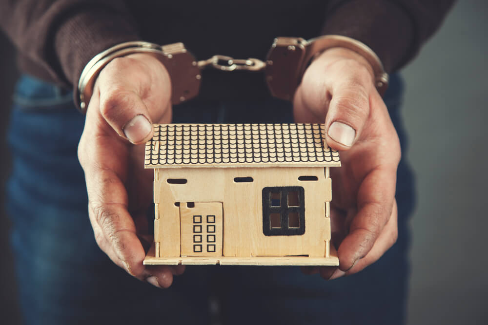 handcuffed hands hold small house to symbolize house arrest
